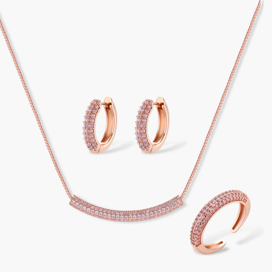 Rose gold jewelry set with pavé cubic zirconia stones including curved necklace, hoop earrings, and adjustable ring on cream background.