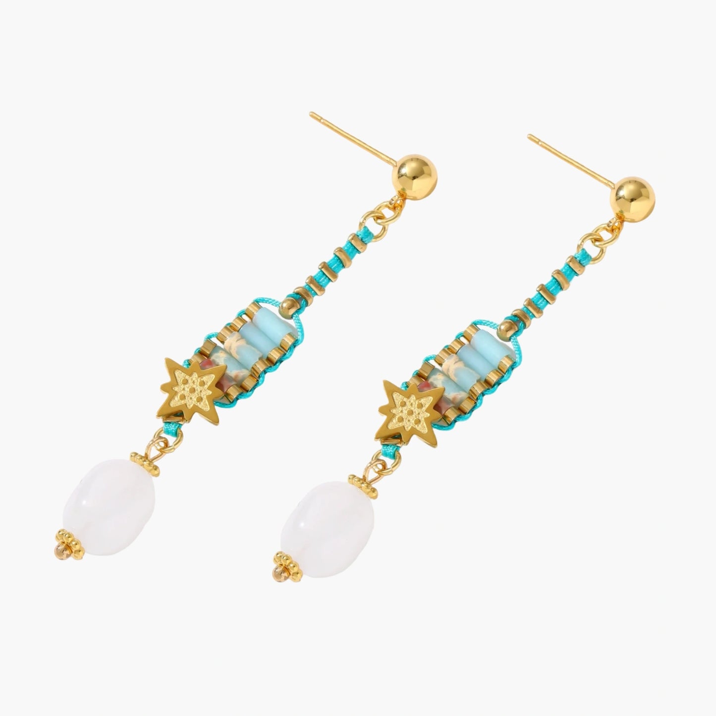 Gold-plated dangle earrings with turquoise threading, star charms, and white pearl beads against cream background.