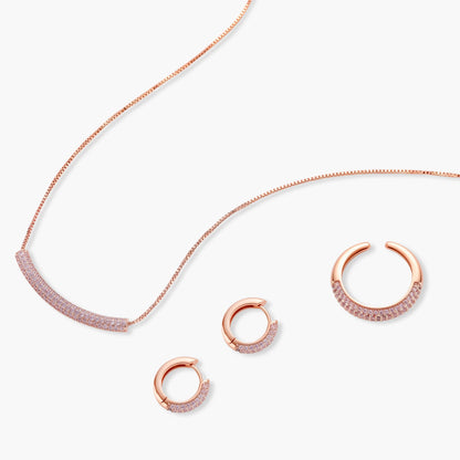 Rose gold jewelry set with pavé cubic zirconia stones including curved necklace, hoop earrings, and adjustable ring on cream background.