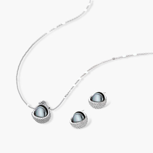 Elegant spherical pendant necklace and earrings set featuring crystal-pavé bottom half in gold or silver finish on white background.